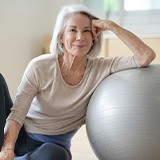 Senior woman smiling while resting against balance ball