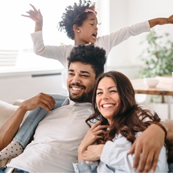 Family of three smiling on the sofa, daughter on dad’s shoulders