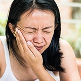 woman in white tank top holding mouth in pain