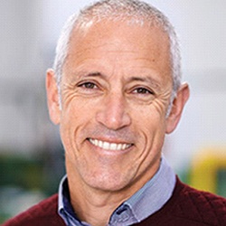 Older man in collared shirt and sweater smiling