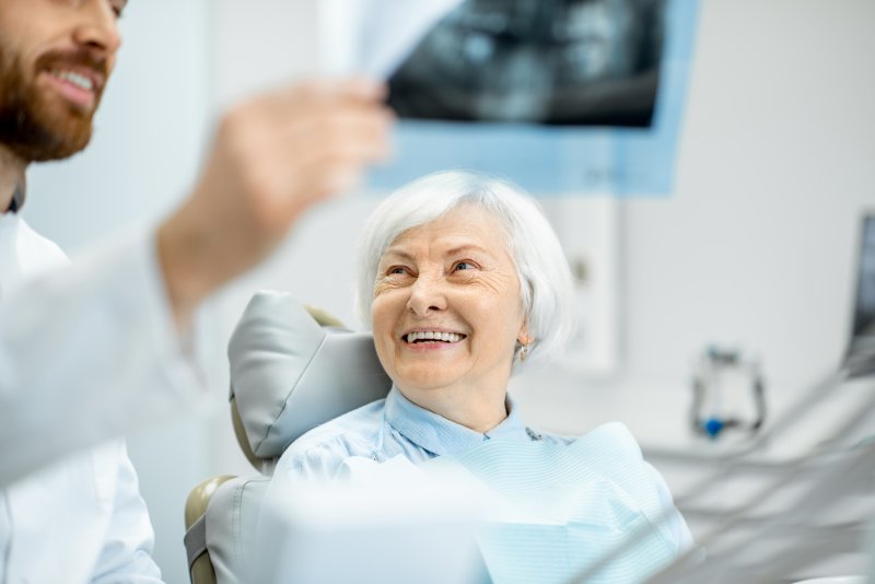 an older woman smiling at her dentist while he explains the process for receiving a dental implant in La Porte