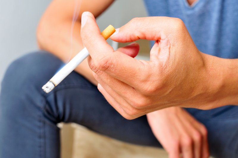 A closeup of a young man’s hand holding a cigarette