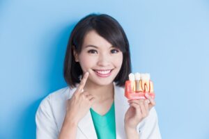 Dentist holding dental implant model and pointing to her own smile.